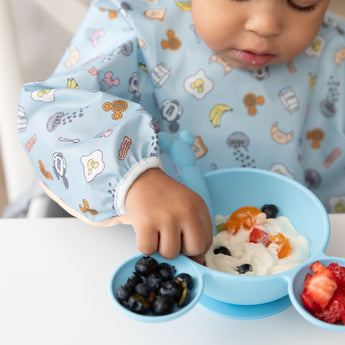 Close-up of a child enjoying baby-led weaning with Bumkins On-The-Go Mealtime 5-Piece Set: Mickey + Minnie Mouse Sunny Side Up Blue.