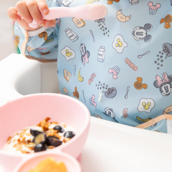 Close-up of a child eating breakfast with Bumkins On-The-Go Mealtime 5-Piece Set: Mickey + Minnie Mouse Sunny Side Up Pink.