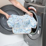 A person holds a Bumkins Sleeved Bib: Mickey + Minnie Sunny Side Up in front of a front-load washer.
