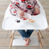 A young girl wearing a Bumkins Sleeved Bib: Minnie Mouse in a highchair eating from the Silicone First Feeding Set: Vanilla Sprinkle.