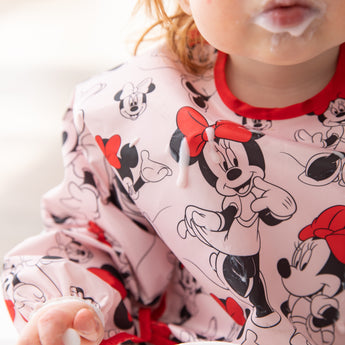 Close-up of a child with a messy mouth wearing a Bumkins Sleeved Bib: Minnie Mouse covered with yogurt drops.