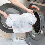 A person holds a Bumkins Sleeved Bib 2 Pack: Disco Boots in front of an open front-loading washing machine.