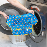 A person holds a Bumkins Sleeved Bib 2 Pack: Mickey & Friends Excellent Eight in front of an open front-loading washing machine.