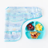 A Bumkins Sleeved Bib 2 Pack: Stitch Star-ring Up Trouble lays folded next to a blue plate with waffles, eggs, & berries on a white background.