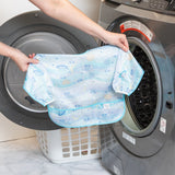 A person holds a Bumkins Sleeved Bib 2 Pack: Stitch Star-ring Up Trouble in front of an open front-loading washing machine.