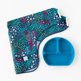 A folded Bumkins Sleeved Bib 2 Pack: Jungle and Animal Print rests near a blue divided plate on a white background.