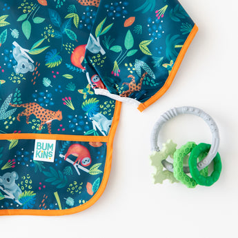 Bumkins Silicone Teething Charms: Green  lays next to a blue animal-patterned sleeved bib on a white background.