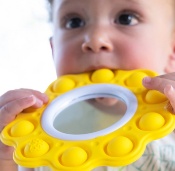 A child engages with the Dimpl Billow Bright by Fat Brain Toy Co, enjoying its yellow bubbles and mirror to boost fine motor skills.