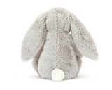 A Jellycat, Blossom Bunny Silver plush with long ears sits facing away, displaying its fluffy white tail.