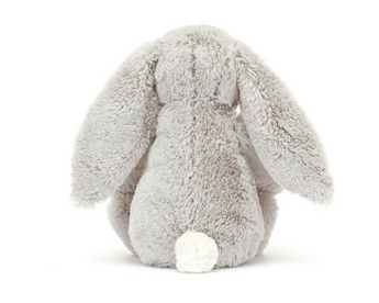 A Jellycat, Blossom Bunny Silver plush with long ears sits facing away, displaying its fluffy white tail.