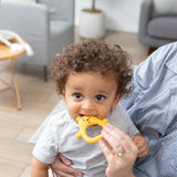 A baby with curly hair chews on a Bumkins Silicone Flat Teether: Winnie the Pooh, soothing gums while being held indoors.