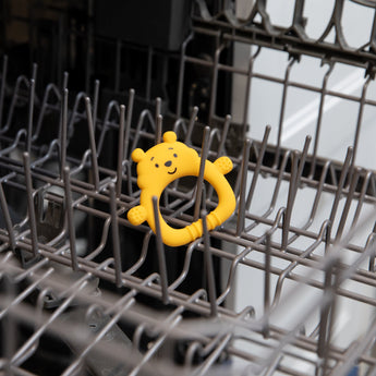 Bumkins Silicone Flat Teether: Winnie the Pooh sits in the top rack of an open dishwasher.