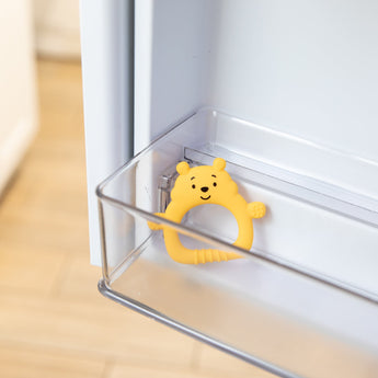 Bumkins Silicone Flat Teether: Winnie the Pooh sits in the side compartment of an open refrigerator door.
