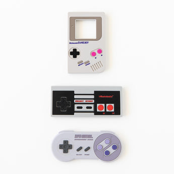 Bumkins Silicone Teether: NES™ Controller rests in between two other game controller shaped teethers on a white background.