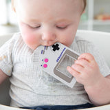 Close-up of a baby in a gray shirt chewing on a Bumkins Silicone Teether: Game Boy™.