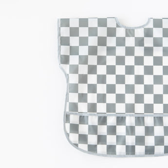 Bumkins Junior Bib: Charcoal Check, with easy-wipe waterproof fabric and a curved neckline, lays flat on a white background.