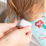 Adult hands adjust the hook-and-loop closure of Bumkins Junior Bib: Ariel around a child's neck.