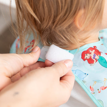 Adult hands adjust the hook-and-loop closure of Bumkins Junior Bib: Ariel around a child's neck.