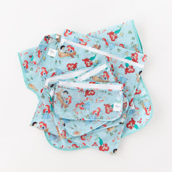 Bumkins Junior Bib: Ariel lays on a white background underneath bags with a matching print.