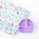 Bumkins Junior Bib: Disney Aloha Stitch lays flat next to a purple divided plate on a white background.