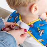 Adult fastening a Bumkins Junior Bib 2 Pack: Mickey & Friends Excellent Eight with Velcro around a young childs neck.