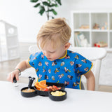 A young child wears the Bumkins Junior Bib 2 Pack: Mickey & Friends Excellent Eight while eating at a white table in a bright room.