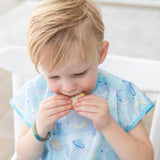 A blonde toddler eats a cookie while wearing a Bumkins Junior Bib 2 Pack: Stitch Star-ring Up Trouble.