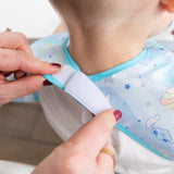 Adult hands fasten the hook-and-loop closure of a Bumkins Junior Bib 2 Pack: Stitch Star-ring Up Trouble around a child's neck.