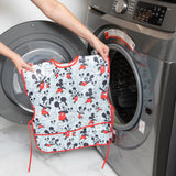 A person holds a Bumkins Short-Sleeved Smock: Mickey Mouse Classic in front of an open front-loading washing machine.