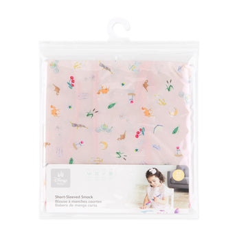 Bumkins Short-Sleeved Smock: Princess Magic is shown folded in a plastic packaging bag with a hanger and cardboard insert.
