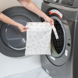 A person holds a Bumkins Wet Bag 2 Pack: Palm Check in front of an open front-loading washing machine.