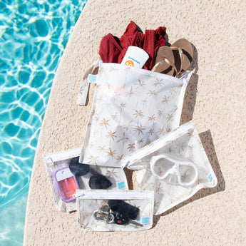 Bumkins The Chaos Coordinator Essential 4-Piece Set: Palm Daze holds swim gear and more on a tan deck next to a blue pool.