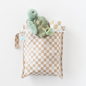 Bumkins Wet Bag + Wet/Dry Bag Set in Sand Check holds a plush turtle, pacifier, and essentials; all on a white background.