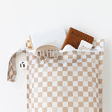 A bag from Bumkins The Chaos Coordinator Essential 4-Piece Set: Sand Check holds a passport, notebook, and more on a white background.
