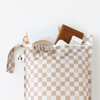 A bag from Bumkins The Chaos Coordinator Essential 4-Piece Set: Sand Check holds a passport, notebook, and more on a white background.