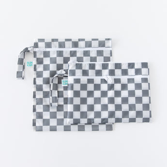 Two bags from Bumkins The Chaos Coordinator Deluxe 5-Piece Set: Charcoal Check lay overlapped on a white background.