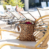 A bag from Roamio by Bumkins The Commuter Essential 4-Piece Set: Leopard sits on a rattan lounge chair with beach essentials inside.