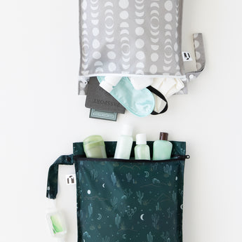 Roamio by Bumkins Wet Bag 2 Pack: Desert Night is neatly arranged on a white background with toiletries and travel essentials inside.