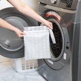A person holds a bag from Bumkins The Chaos Coordinator Essential 4-Piece Set: Lunar Phase in front of an open front-loading washing machine.
