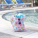 A bag from Bumkins The Playdate Planner Deluxe 5-Piece Set: Boots holds a towel, a bottle & pink sunglasses by a pool.