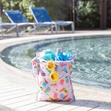 A bag from Bumkins The Playdate Planner Deluxe 5-Piece Set: Boots holds sunglasses and swim gear poolside with empty lounge chairs behind.