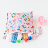 Travel-size toiletries and a hairbrush spill from an open Roamio by Bumkins Wet Bag: Boots on a white background.