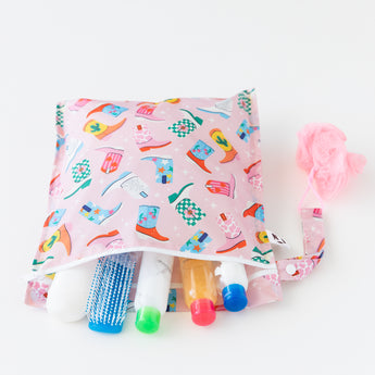 Travel-size toiletries spill out of an open bag from Bumkins The Chaos Coordinator Essential 4-Piece Set: Boots on a white background.
