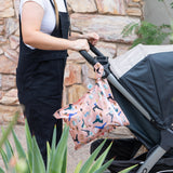 A person in black overalls pushes a stroller with a Bumkins Wet Bag: Yoga Pals hanging from the handle against a stone wall.