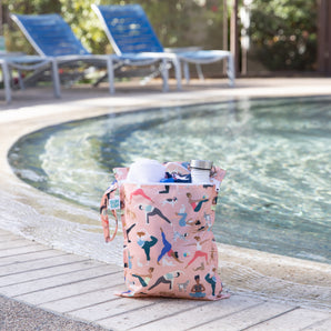 The Bumkins Wet Bag + Wet/Dry Bag Set: Yoga Pals rests poolside with a towel, bottle, lounge chairs, and greenery behind.