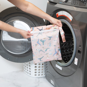 A person holds a Bumkins Wet Bag: Yoga Pals in front of an open front-loading washing machine.