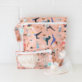 Bumkins Wet Bag: Yoga Pals sits on a white table against a white brick wall, with breast pump parts and a matching bag in front.