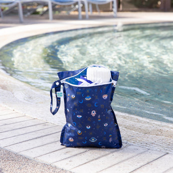 A bag from Bumkins Wet Bag + Wet/Dry Bag Set: Evil Eye holds a towel and swim gear poolside.