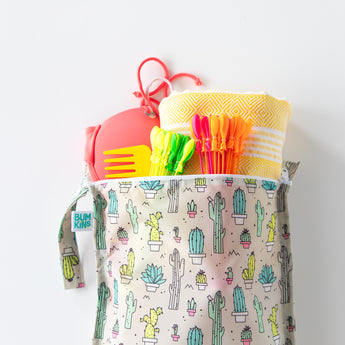 Bumkins Wet Bag: Cacti holds a towel, swimsuit, and colorful pool toys on a white background.