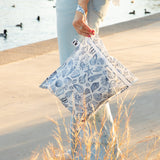 A woman holds a bag from Roamio by Bumkins The Commuter Essential 4-Piece Set: Shells on a concrete path; water with ducks behind.